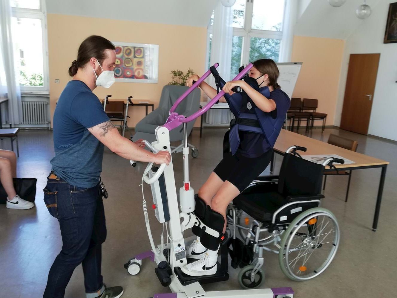 Schülerin mit Trainingsgerät und Rollstuhl mit Betreuer