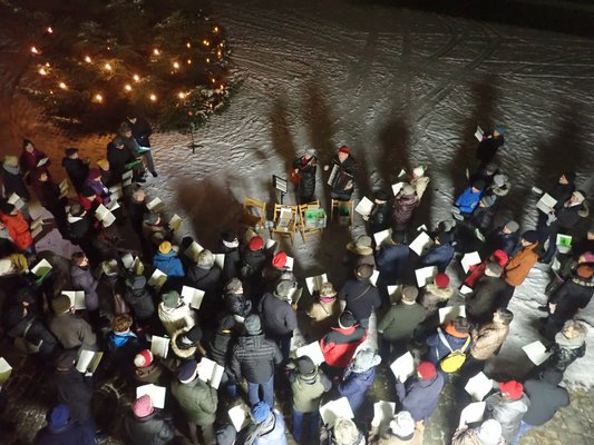 Eine Menschenmenge steht draußen zusammen und singt Weihnachtslieder