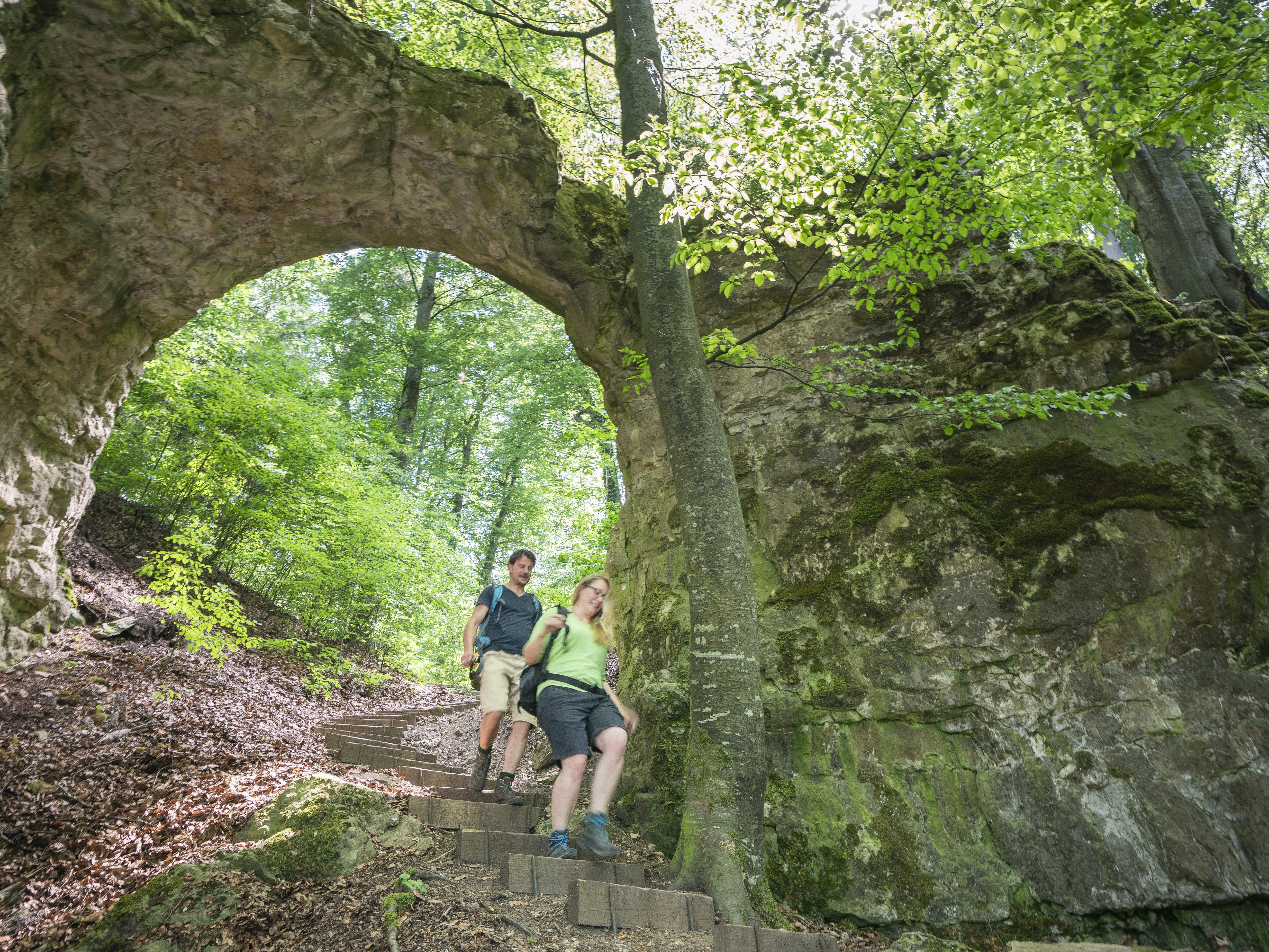 Zwei Wanderer im Wald gehen durch ein Felsentor