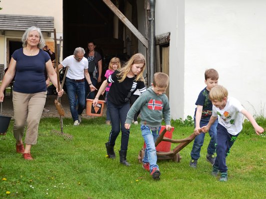Kinder und Erwachsene laufen mit Gartengeräten auf die Wiese