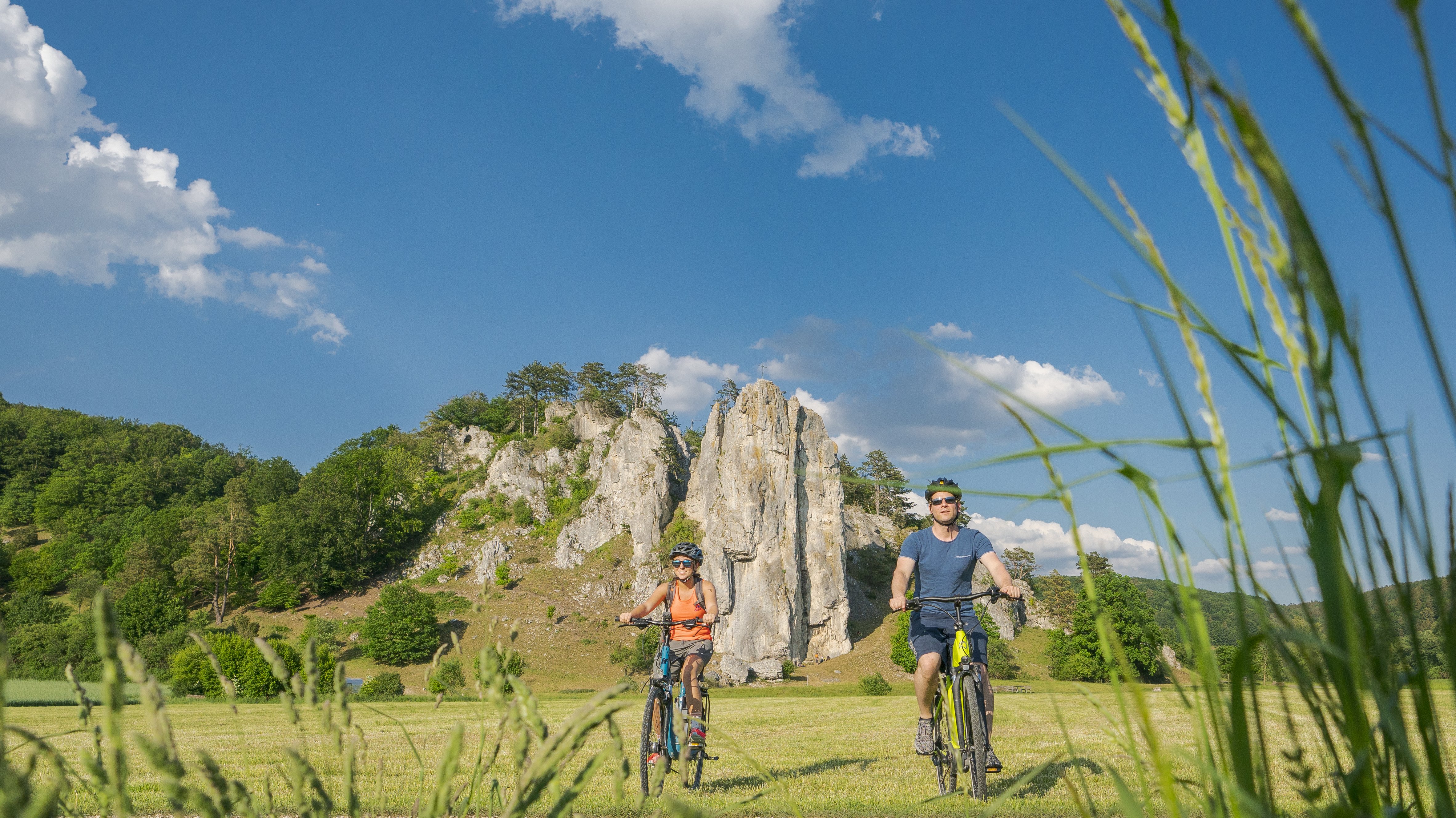 Zwei Radfahrer in der Natur vor Felsen, Grün und blauem Himmel